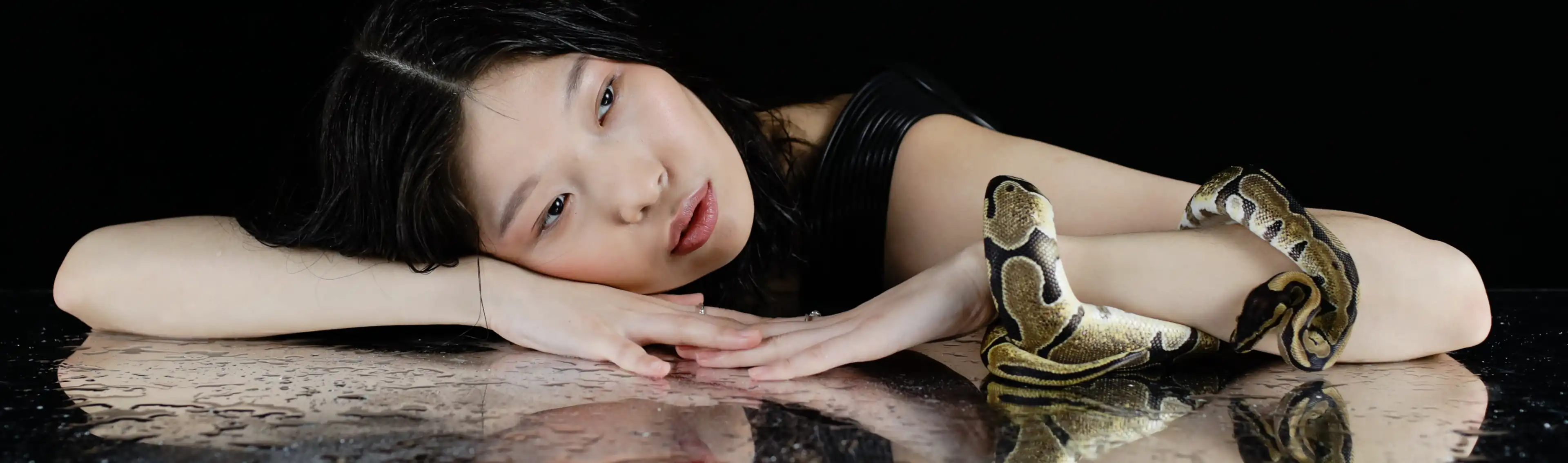 A woman lying on her arm in a mirror table, a snake in front of her